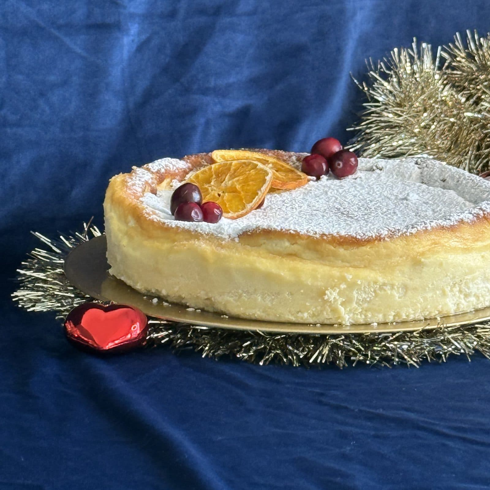 Sernik puszysty posypany cukrem pudrem, ozdobiony suszoną pomarańczą i żurawiną